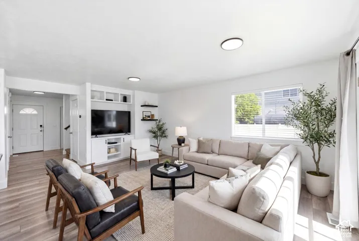 Open-concept living area with wood-finish flooring, a white trim entry door featuring an arched window, and a built-in media console with open shelving