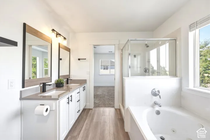Double vanity featuring rectangular sinks with matte black faucets, wood-finish flooring, a jetted soaking tub, and a separate glass-enclosed shower
