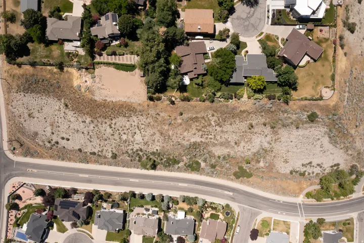 Expansive undeveloped parcel featuring natural ground cover, bordered by established residential properties and a paved road