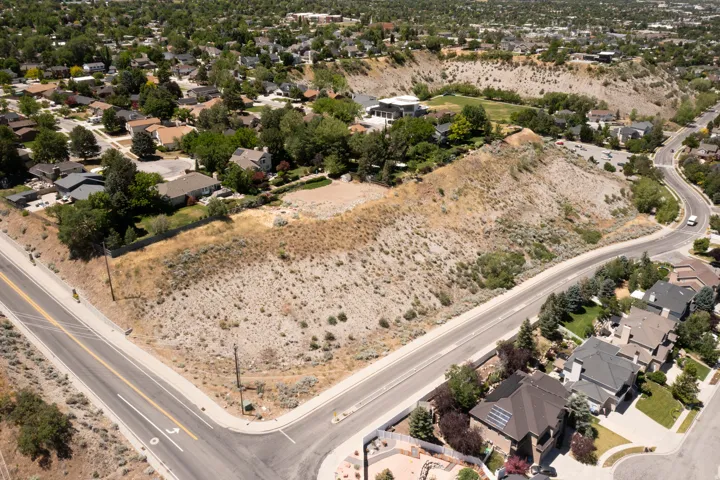 Expansive parcel of undeveloped land situated at a road intersection, bordered by established residential properties