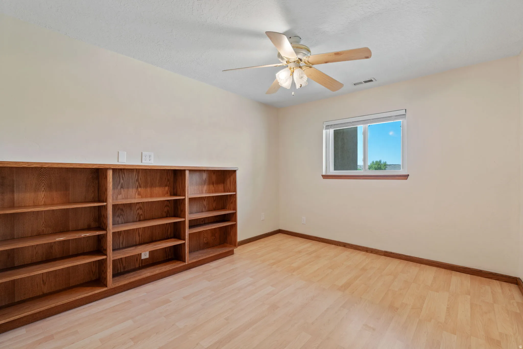 Room featuring built-in wood shelving, light wood-finish flooring, and a ceiling fan with integrated lighting