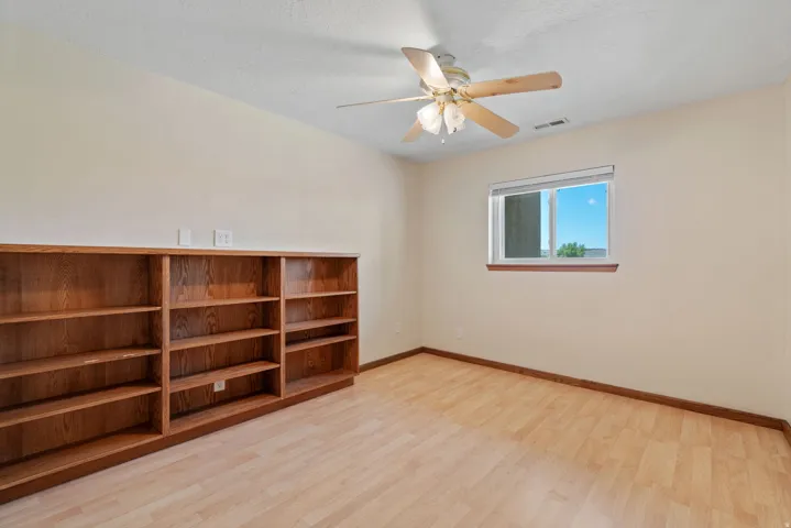 Room featuring built-in wood shelving, light wood-finish flooring, and a ceiling fan with integrated lighting