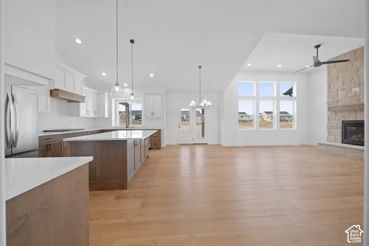 Open-concept living space featuring a gourmet kitchen with stainless steel appliances, a large central island with seating, wood-finish flooring, a stone-clad fireplace with a wood mantle, and expansive windows