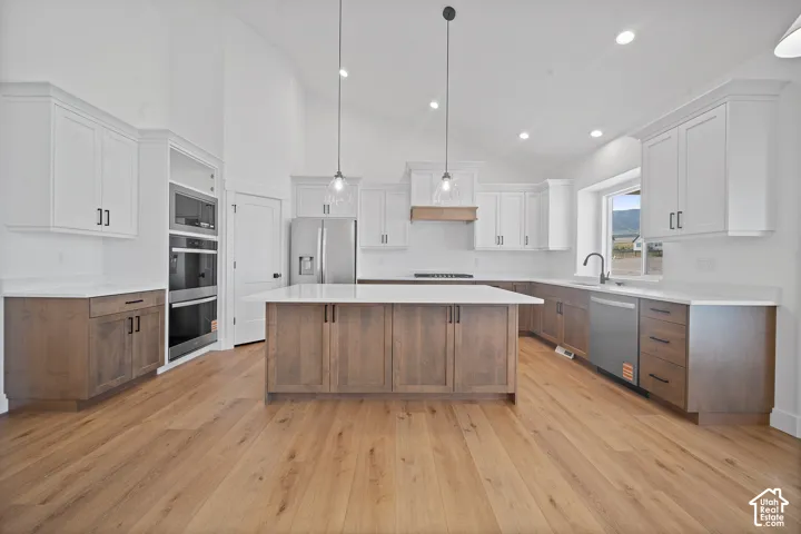 Modern kitchen featuring a large central island, light wood-finish flooring, and vaulted ceilings
