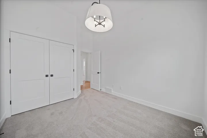 Spacious room featuring light gray carpeting, tall white baseboards, and a contemporary ceiling light fixture