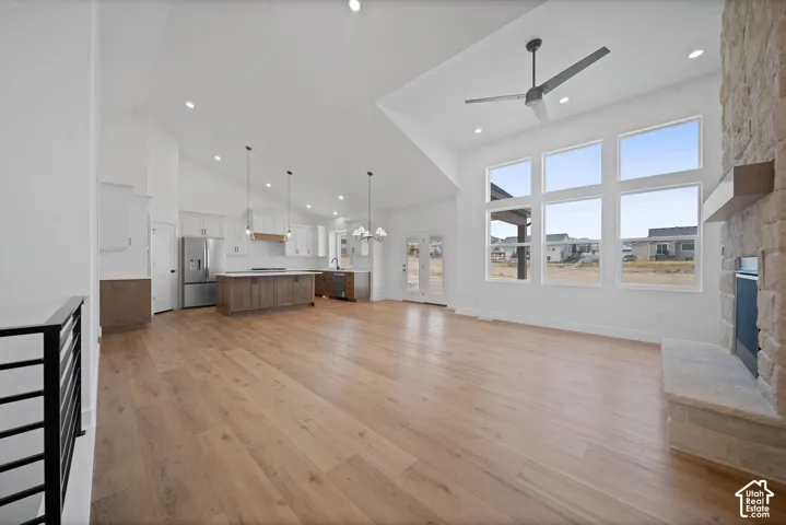 Expansive open-concept living space featuring wood-finish flooring, a stone-clad fireplace, and a vaulted ceiling with a modern ceiling fan