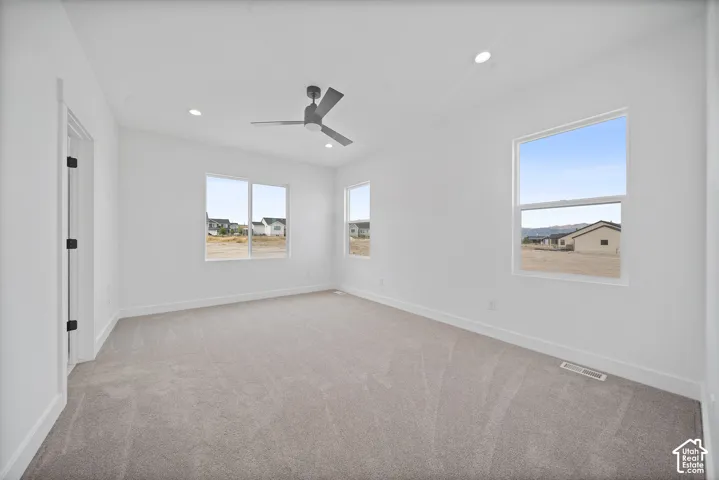 Spacious room featuring light gray carpeting, crisp white walls, multiple windows, a contemporary ceiling fan, and recessed lighting