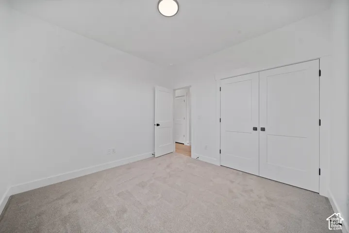 Spacious room featuring light-colored carpeting, white baseboards, and bright white walls