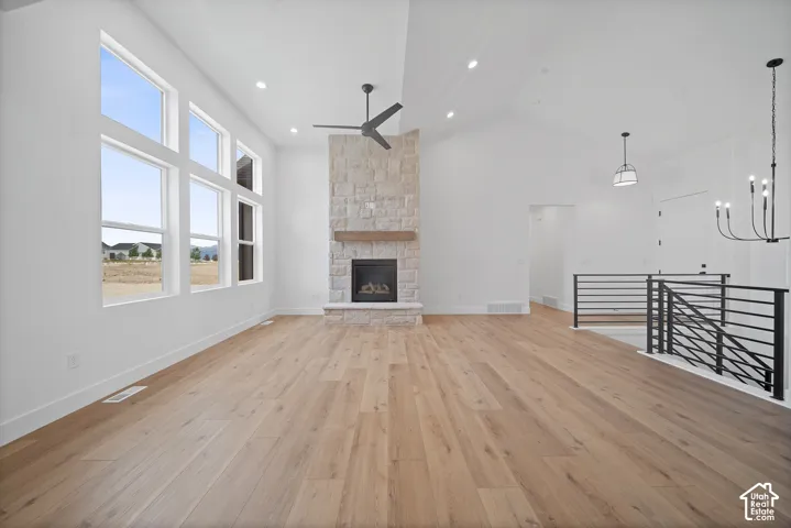 Spacious living area featuring high vaulted ceilings, expansive multi-pane windows, a stone-clad fireplace with a wood mantel, wood-finish flooring, and a modern black metal railing