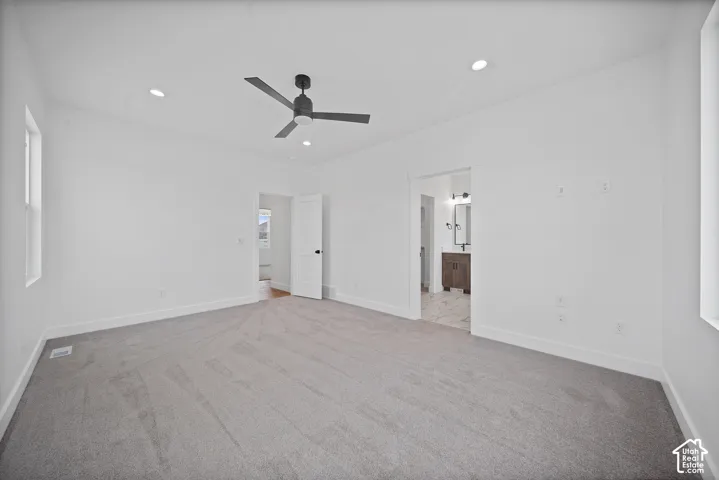 Spacious room featuring light gray carpeting, crisp white walls, and a contemporary black ceiling fan