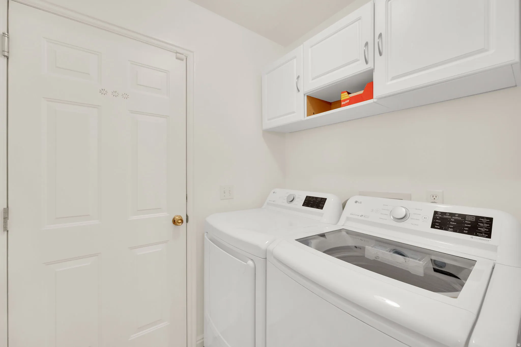 Dedicated laundry area featuring white upper cabinetry, a paneled door, and neutral wall tones