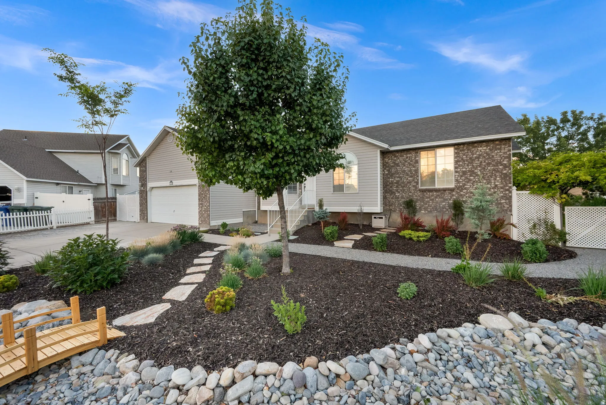 Exterior featuring a mix of brick and siding, a gravel pathway, and a stone-lined planter with varied landscaping