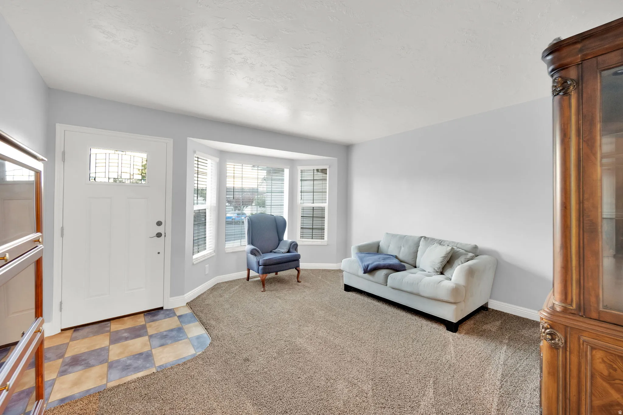 Inviting entryway featuring a white paneled door with glass insert, bay windows, checkered tile flooring, and neutral carpeting