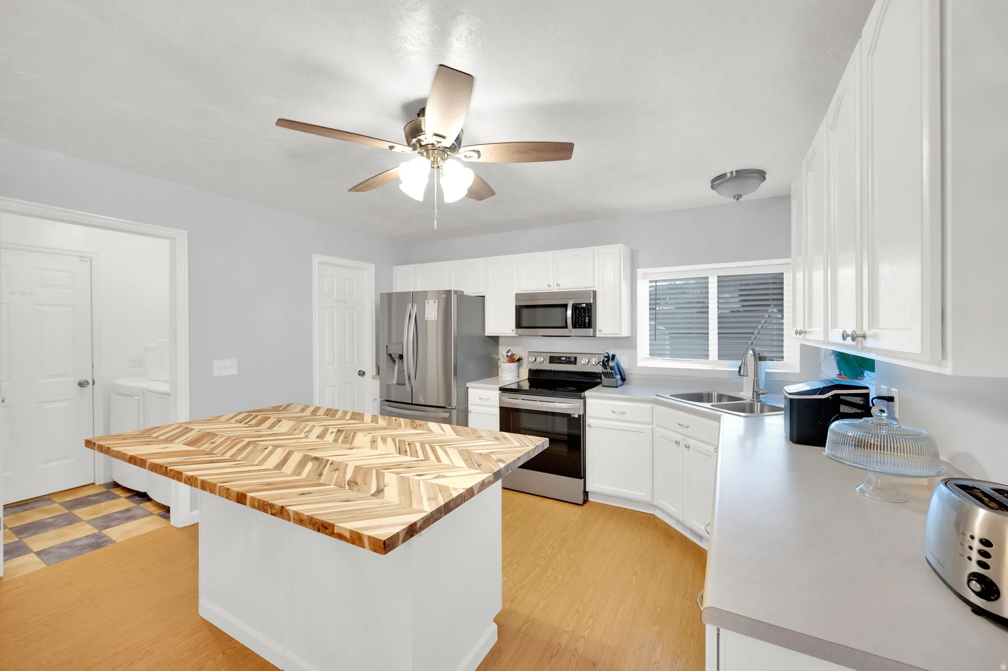 Kitchen featuring a custom wood-patterned island, white cabinetry, light countertops, stainless steel appliances, and wood-finish flooring