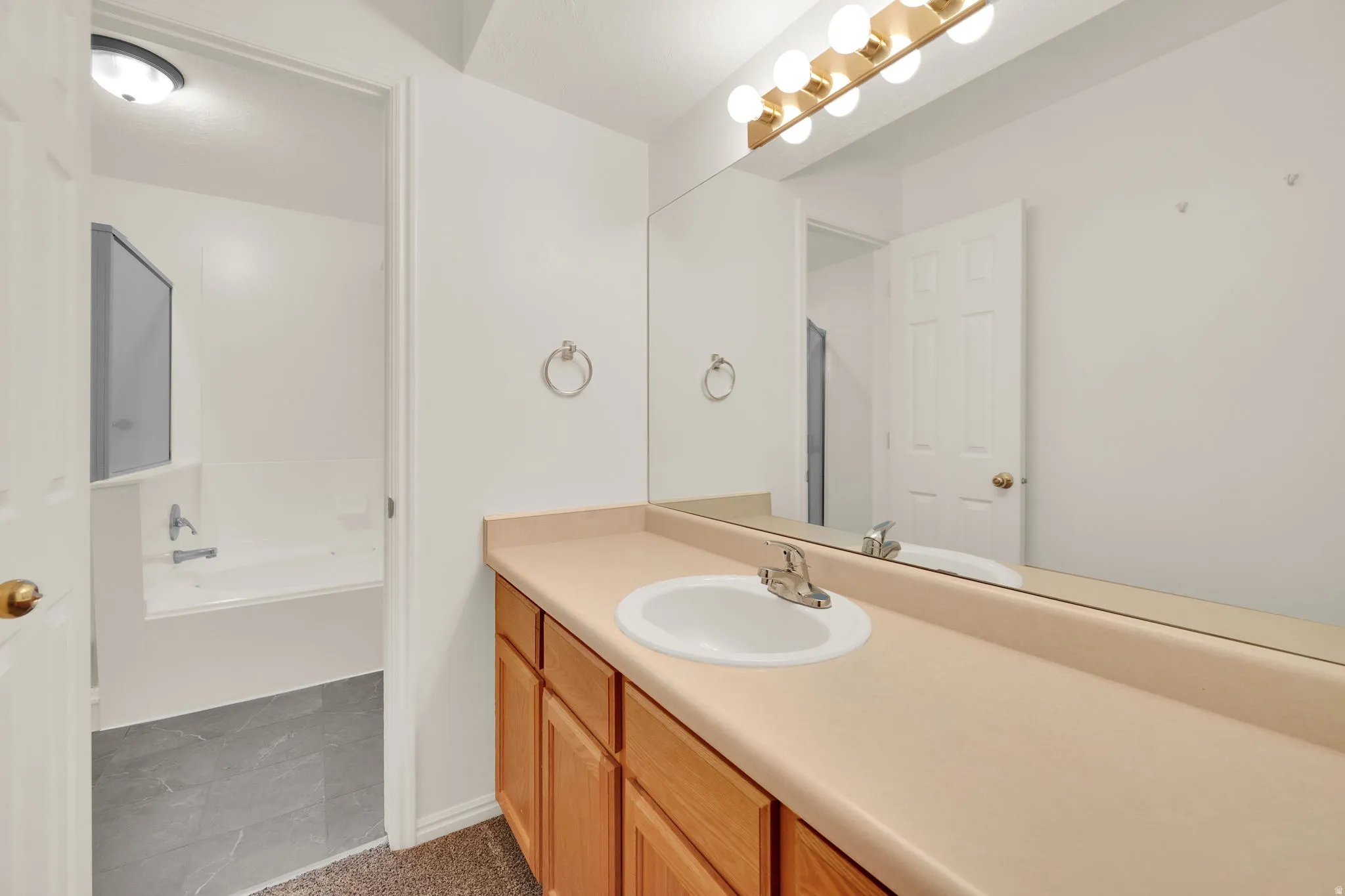 Bathroom vanity with light wood-finish cabinetry, a single basin sink, and a spacious countertop