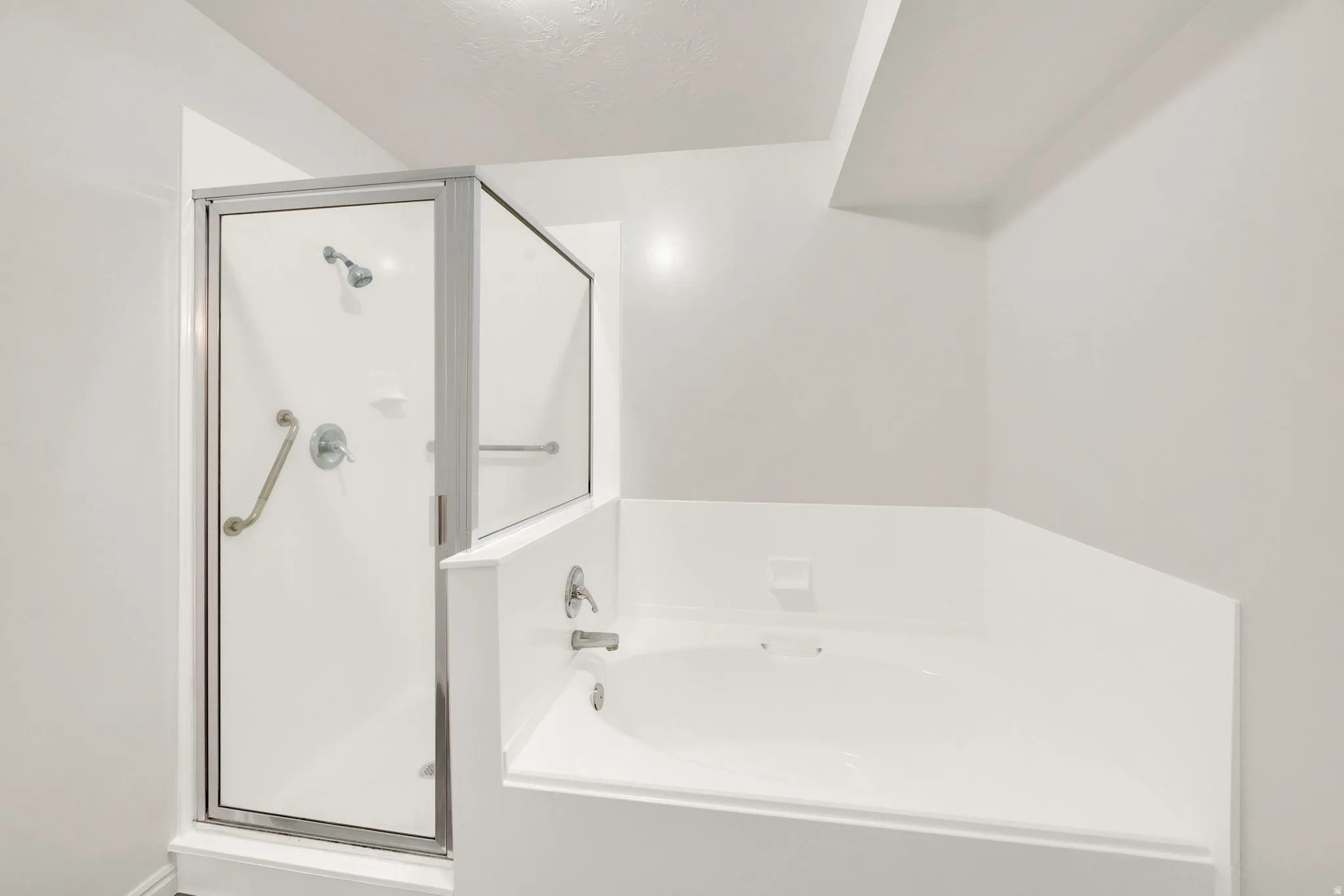 White soaking tub with integrated surround, accompanied by a glass-enclosed shower with grab bars and a chrome shower head