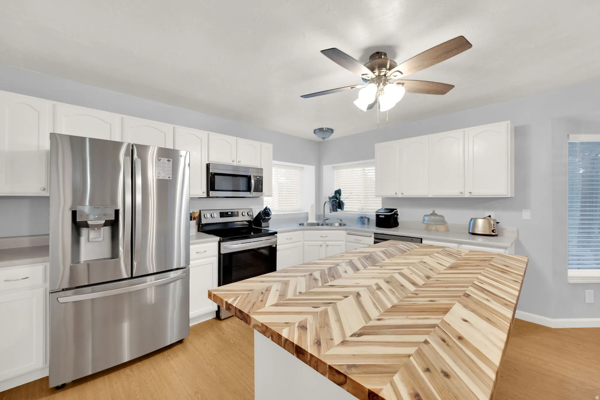 Kitchen featuring a chevron-patterned wood island countertop, stainless steel appliances including a French door refrigerator and built-in microwave, white cabinetry, light countertops, and wood-finish flooring