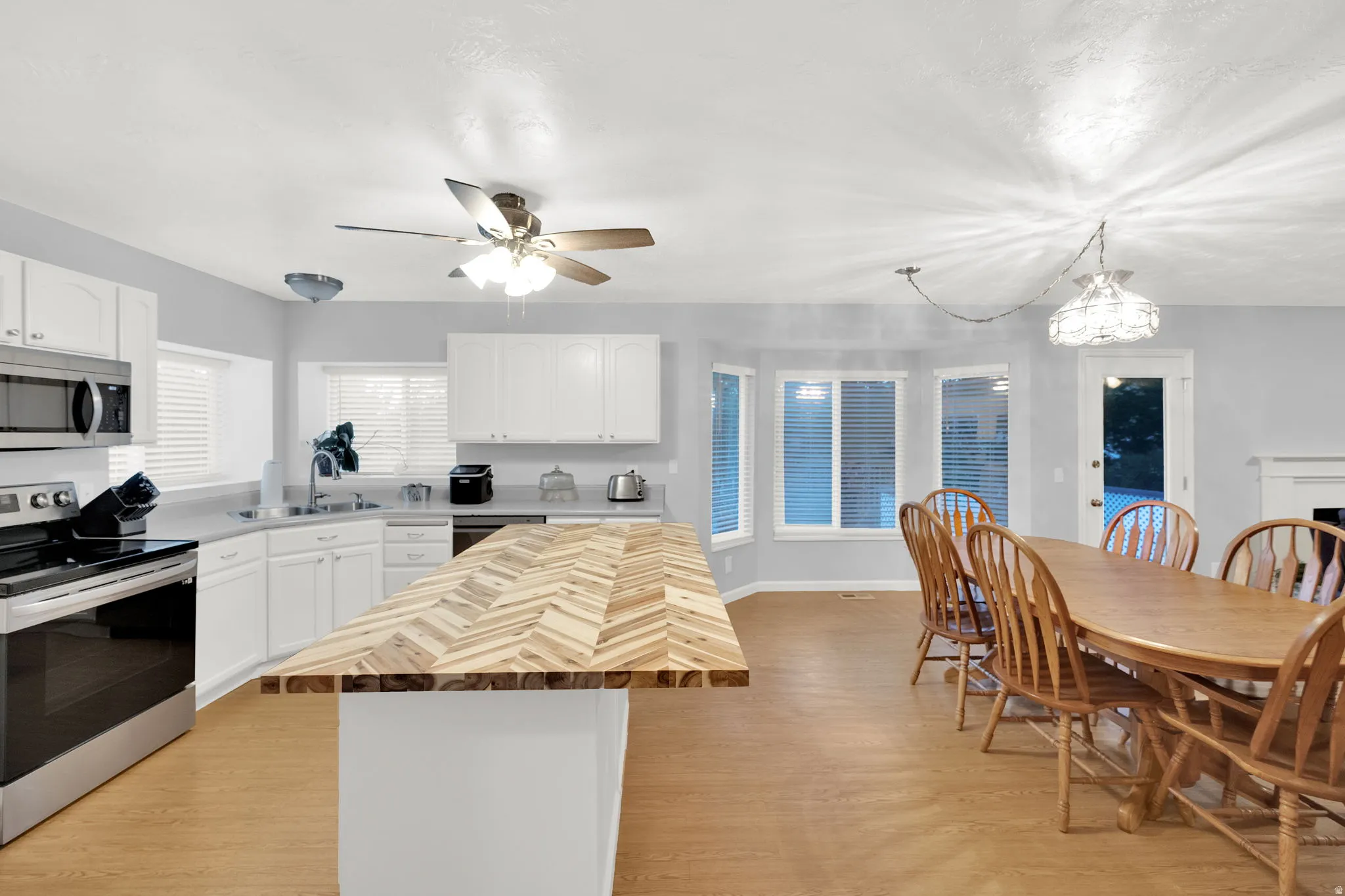 Kitchen featuring white cabinetry, stainless steel appliances, a chevron pattern wood-finish island countertop, and light wood-finish flooring
