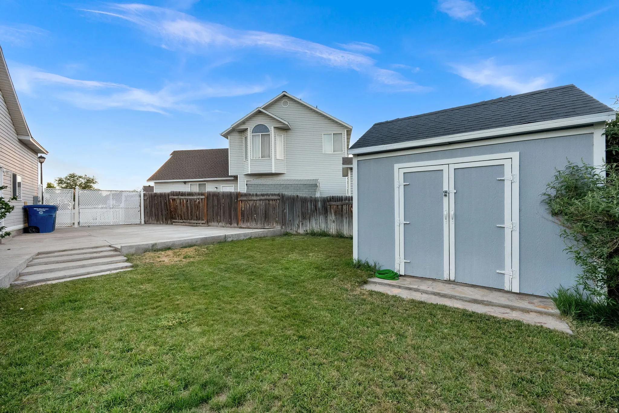 Spacious backyard featuring a manicured lawn, a large concrete patio, and a dedicated storage shed with double doors
