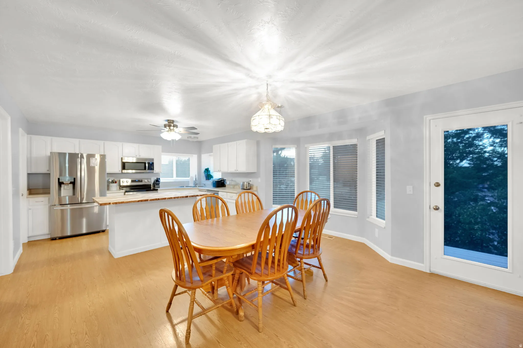 Open-concept kitchen and dining area featuring light-finish flooring, white cabinetry, stainless steel appliances, and a curved window wall