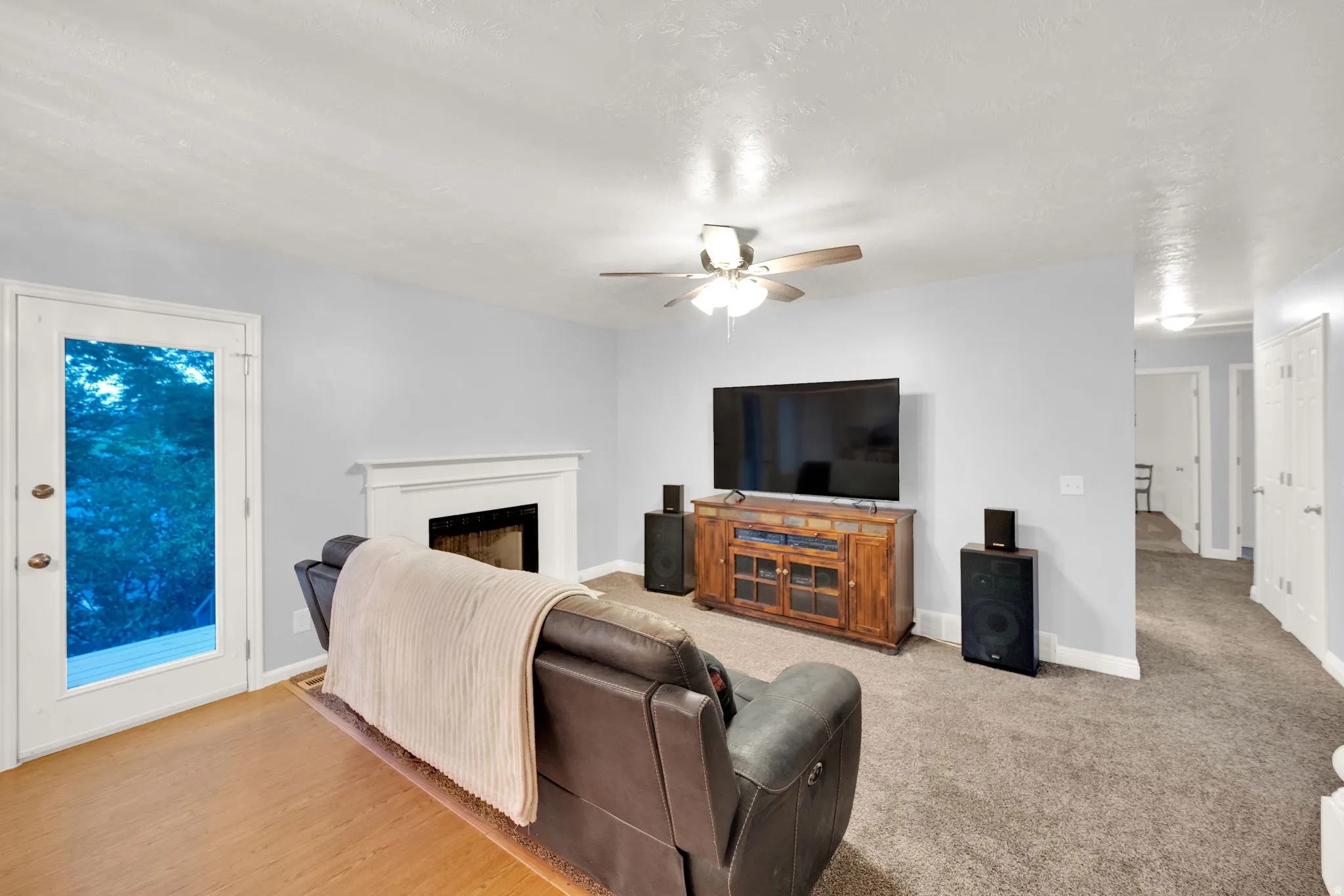 Living area featuring a fireplace with a white mantel, ceiling fan, and carpeted flooring