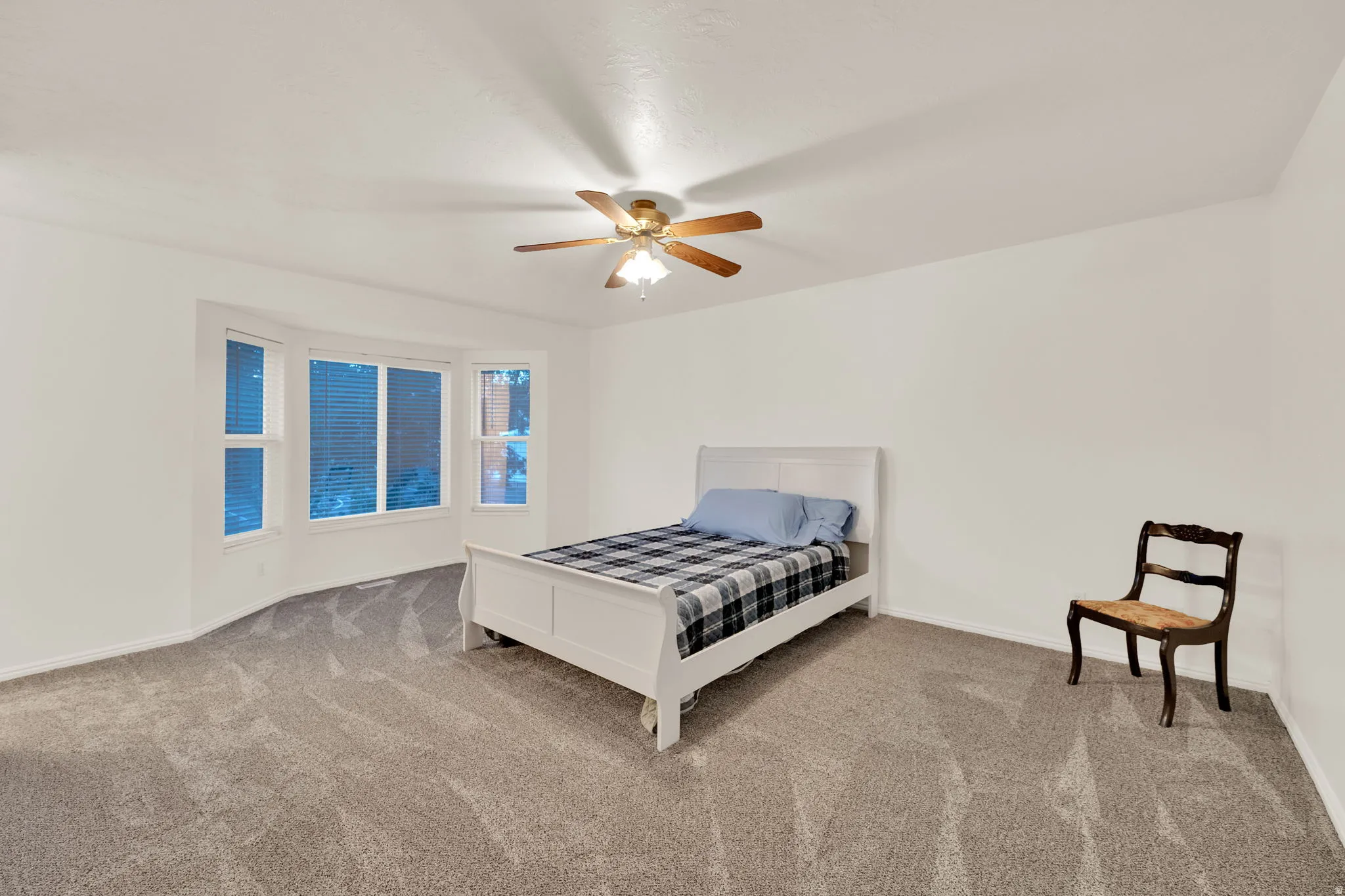 Spacious room featuring a bay window, neutral carpeting, and a ceiling fan with integrated lighting