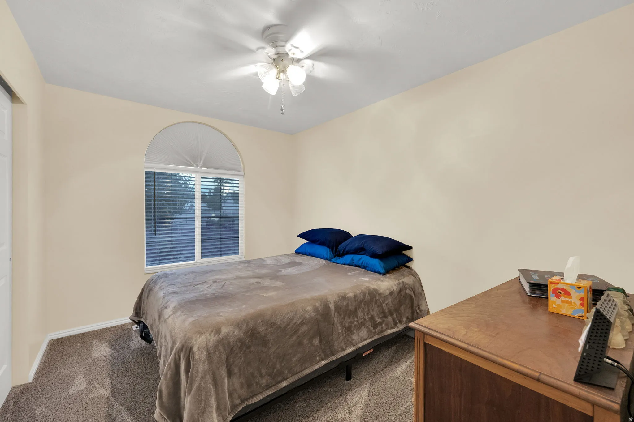 Bedroom featuring a prominent arched window, neutral wall paint, ceiling fan with light fixture, carpeted flooring, and white trim