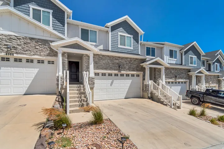 Multi-level townhome featuring a stone and shingle facade, white garage doors, and a covered entry porch with white railings