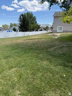 Spacious backyard featuring a white vinyl privacy fence, mature trees, and a mountain backdrop