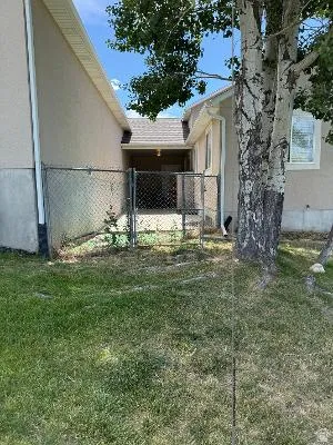 Grassed side yard featuring a chain-link fence and a covered patio area