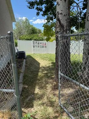 Grassed side yard featuring mature trees and a chain-link fence