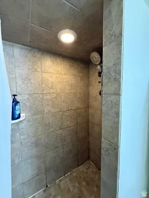 Tiled shower with a recessed ceiling light, wall-mounted showerhead, and an integrated corner shelf