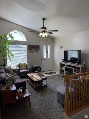 Vaulted ceiling living area featuring a decorative arched window, a ceiling fan with integrated lighting, a front entry door with glass inserts, and wood baluster staircase