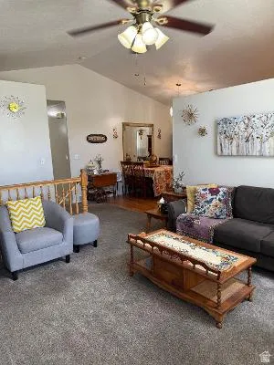 Vaulted ceilings accentuate the living area, featuring textured carpeting and a ceiling fan with integrated lighting