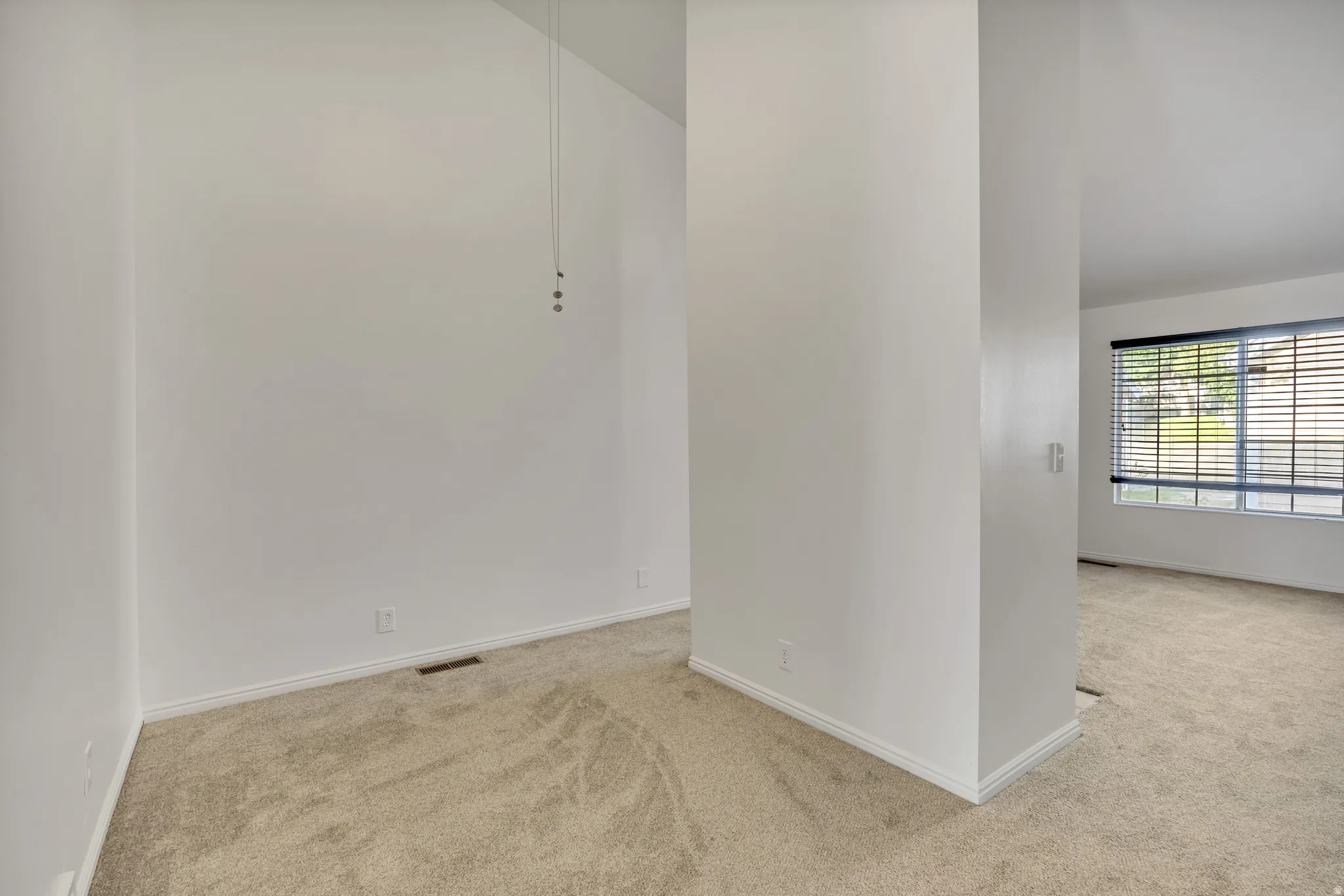 Open room featuring vaulted ceilings, light-toned carpeting, and white baseboards