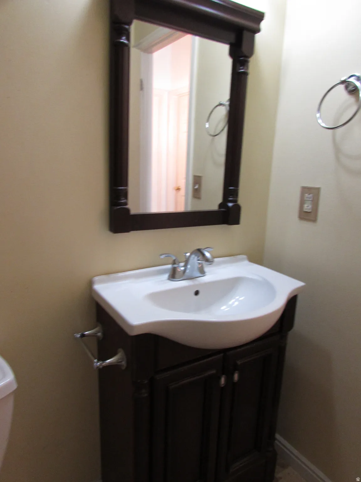 Dark wood-framed mirror above a white integrated sink and dark wood vanity with cabinet storage