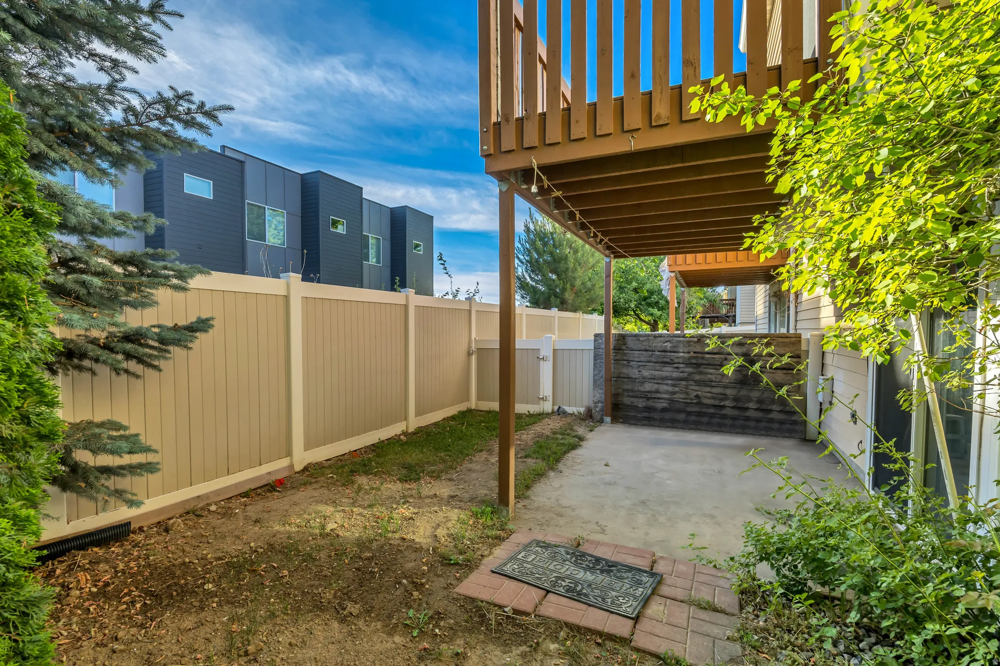 Private outdoor area featuring a vinyl privacy fence, concrete covered patio, and mature landscaping