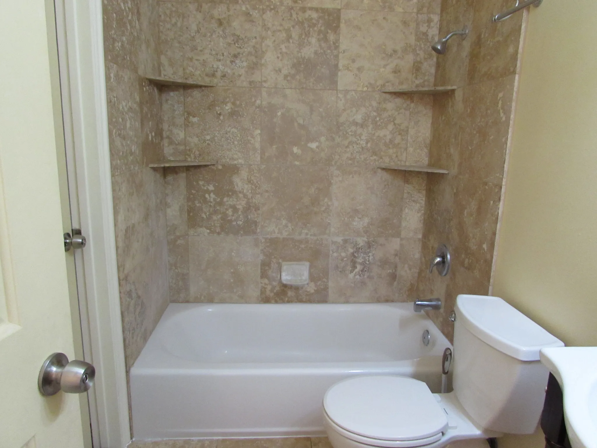 Full bathroom featuring a tub/shower combination with tile surround, built-in shower shelves, and chrome fixtures