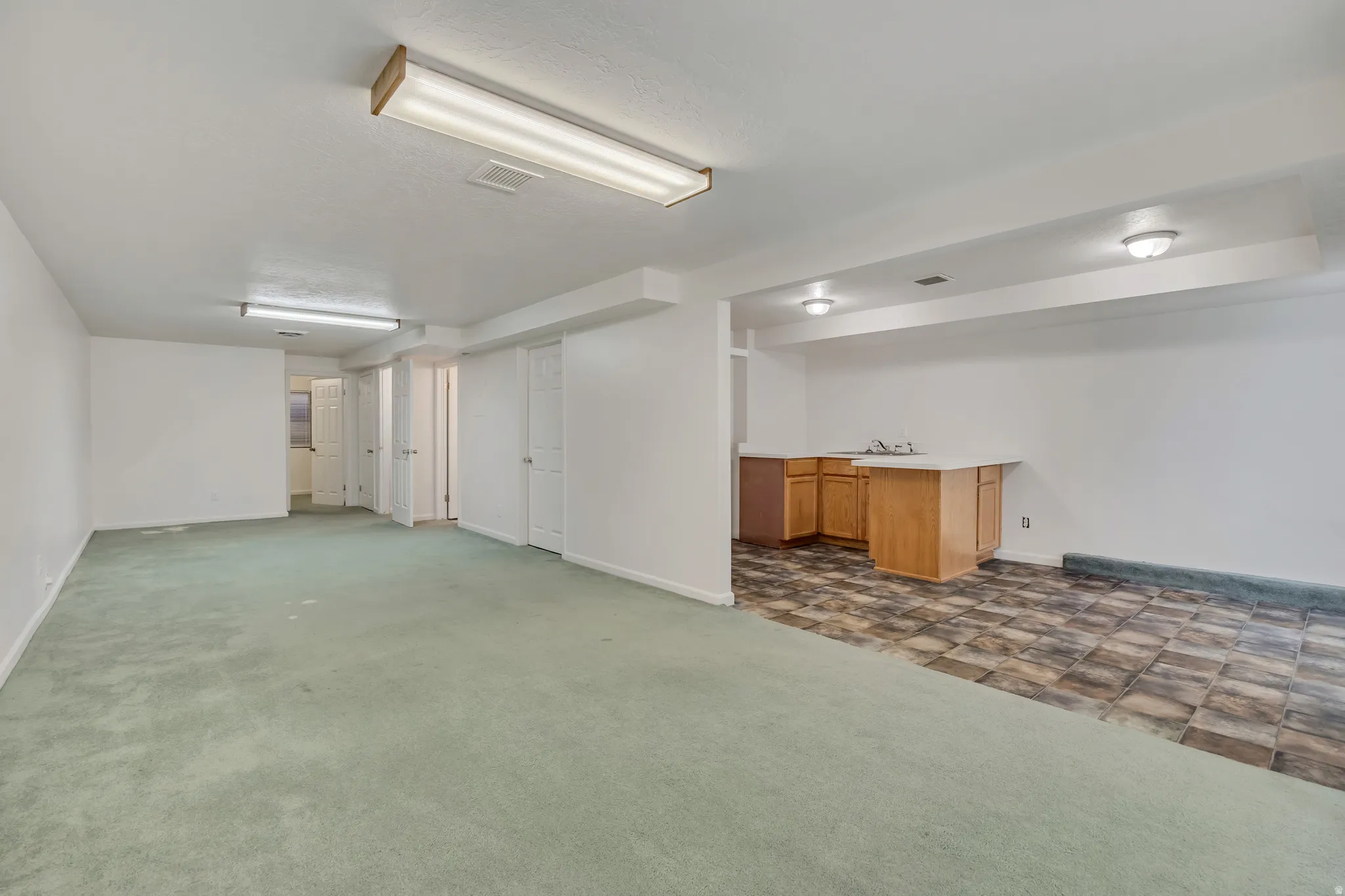 Lower-level area with recessed lighting and fluorescent fixtures and wet bar,