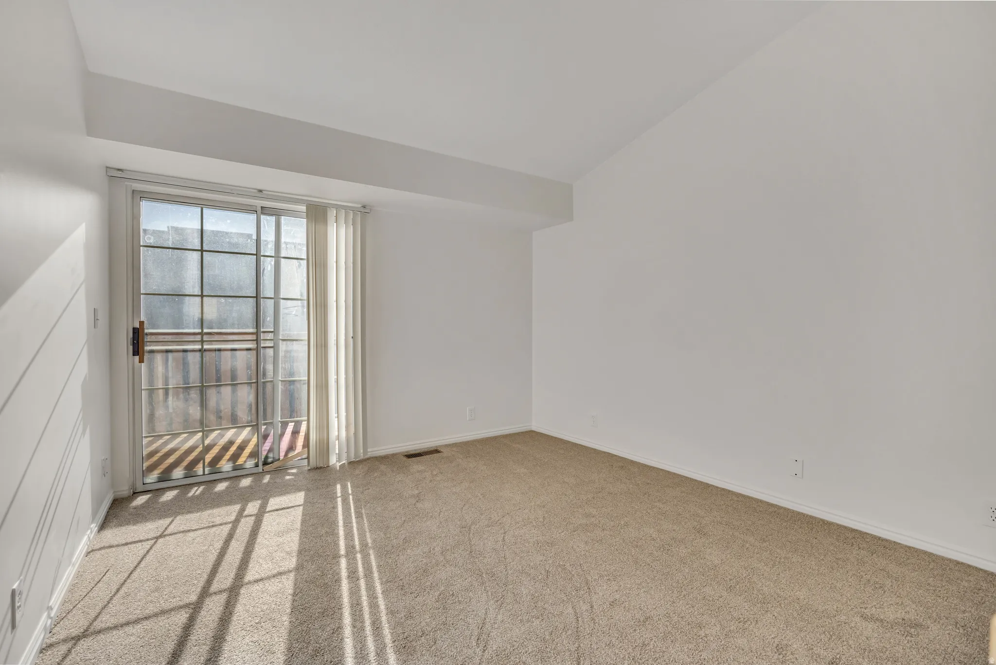 Spacious room featuring a sliding glass door, neutral carpeting, vaulted ceiling, and white wall finishes. Entry to deck.