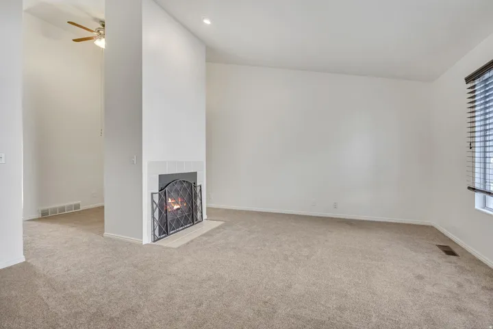 Spacious room featuring a fireplace with a white tile surround and hearth, neutral carpeting, a window with blinds, and a recessed ceiling light