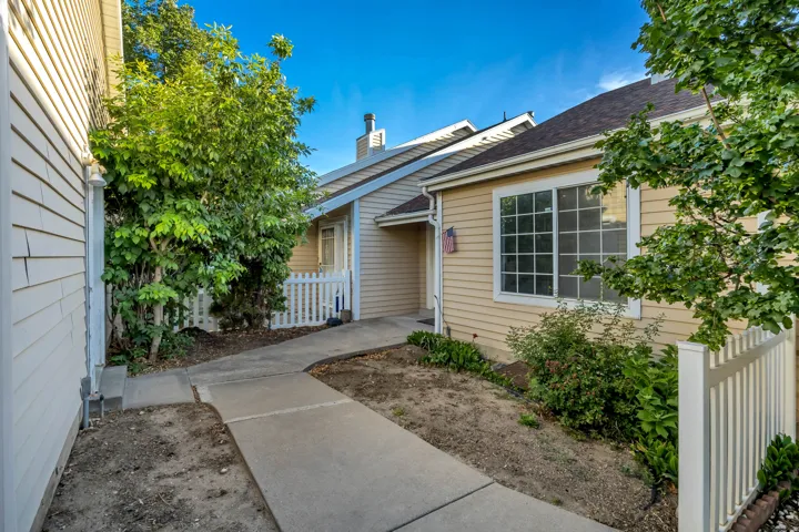 Curb appeal featuring a neutral-toned exterior, a bright white picket fence, mature trees and shrubs, a front entry door with a sidelight, and multi-pane windows