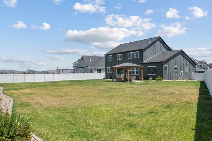 Expansive backyard featuring a large green lawn, full vinyl fencing, and a permanent wooden gazebo with a concrete pad