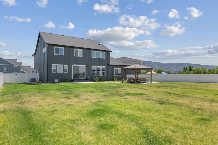 Expansive backyard featuring a gazebo with a concrete pad, a white privacy fence, and mountain scenery
