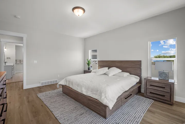 Spacious bedroom featuring light neutral wall tones, wood-finish flooring, a contemporary ceiling light fixture, and a large window providing natural light