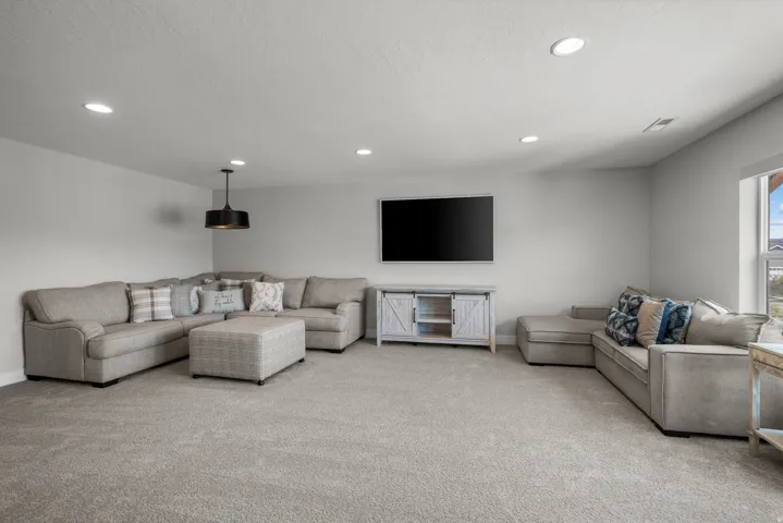 Spacious carpeted room featuring recessed lighting, a ceiling-mounted pendant light, and a window providing natural illumination