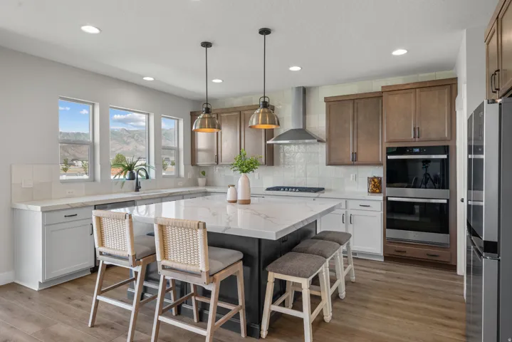 Spacious kitchen featuring a large central island with seating, a stainless steel range hood, double wall ovens, built-in refrigerator, and wood-finish flooring