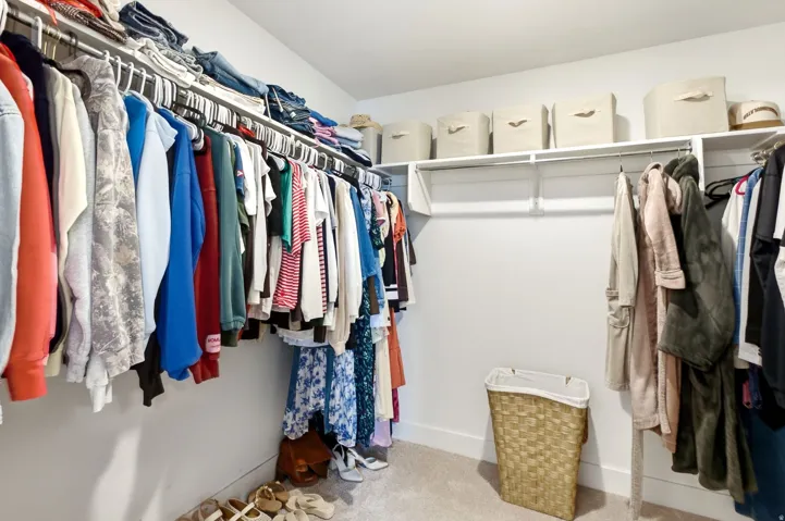 Spacious walk-in closet featuring white wall-mounted shelving and multiple clothing rods for extensive storage