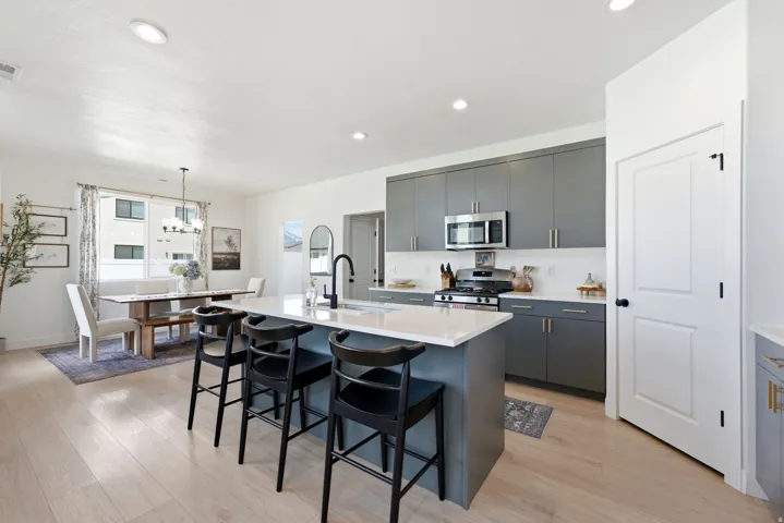 Modern kitchen featuring an island with a light-toned countertop, sleek gray cabinetry, stainless steel appliances, and wood-finish flooring