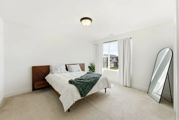 Carpeted bedroom featuring a large window with white curtains, a flush-mount ceiling light fixture, and white painted walls